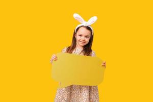 kleines lächelndes Mädchen hält eine gelbe Sprechblase in einem Studio.