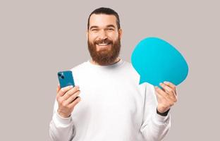 Der junge bärtige Mann hält eine blaue Sprechblase und sein neues Telefon.