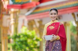 eine schöne thailändische frau in thailändischem kleid mit goldverzierungen hält eine tasse wasser für das songkran-fest oder das thailändische neujahr foto