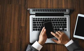 Draufsicht der Hand, die mit Laptop-Computer, Smartphone, Tablet, Kaffeetasse, Stift, Notizblock im Dunkeln im Büro arbeitet foto