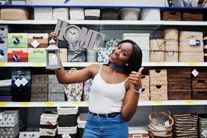 Porträt einer schönen afroamerikanischen Frau, die ein Heimschild und eine Wandleuchte im Laden hält. foto