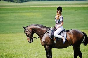 junges hübsches mädchen, das an einem sonnigen tag auf einem feld reitet. foto