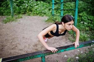 Sportmädchen bei Sportbekleidung, die an horizontalen Stangenübungen in einem grünen Park trainiert und in der Natur trainiert. eine gesunde Lebensweise. foto