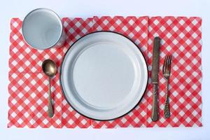 Flaches Picknicktischgedeck aus Teller, Tasse, Besteck und karierter Tischdecke foto