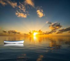 Weißes Ruderboot, das auf dem offenen Meer treibt und in Richtung Sonnenuntergang treibt foto