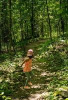 Kleines Mädchen in einem Wald, das mit ängstlicher Haltung auf den Weg zurückblickt foto