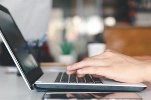 junger mann, der laptop-computer und handy verwendet, wenn er nach finanzinformationen im geschäft sucht, arbeitet am schreibtisch. mit einem Stift schreiben, von zu Hause aus lernen und von zu Hause aus arbeiten. foto