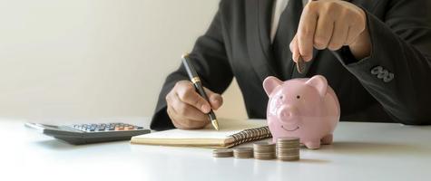 Ein Geschäftsmann legt eine Münze in ein Sparschwein und macht sich Notizen zu den Finanzen. konzept, geld zu sparen und buchhaltungsunterlagen zu prüfen. foto