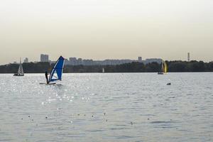 Windsurfer. Mann surft auf dem Hintergrund von Wolkenkratzern. Mann auf einem Windsurfbrett. Windsurfen in der Stadt. Wassersport. Surfen mit einem Segel. Windsurfausrüstung. aktiver Lebensstil. foto