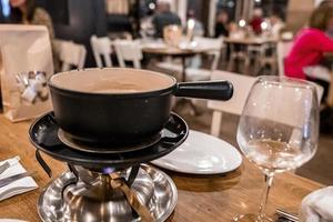 Beheizter Topf mit Schweizer Käsefondue neben Weinglas auf dem Esstisch foto