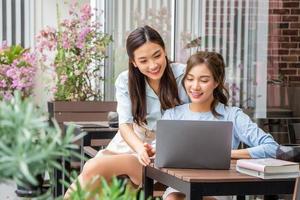 asiatisches Mädchen, das im Laptop schaut, während es mit einer Freundin zusammen im Freien arbeitet foto