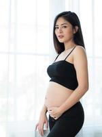 Eine schöne schwangere Frau steht, um ihren Bauch zu fangen foto
