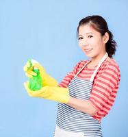 Schöne asiatische Frau, die ein Flaschenspray hält, um das Gerät zu reinigen, und glücklich lächelt, um das Haus zu reinigen