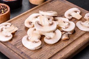 schöne junge weiße champignons, die auf einem dunklen betonhintergrund in scheiben gerissen werden foto