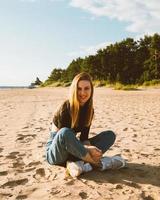 in voller länge schöne lächelnde frau, die abends bei sonnenuntergang am strand sitzt. hübsches Weib foto