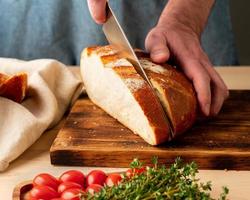 gesichtsloser Mann, der mit einem großen Messer frisches, selbstgebackenes, knuspriges Brot schneidet foto