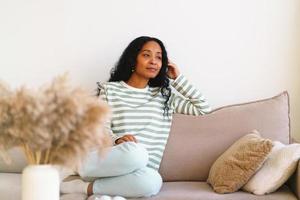 glückliche afroamerikanische frau, die auf sofa im wohnzimmer sitzt foto