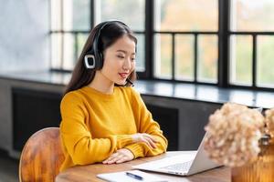 asiatische frau im headset, die per konferenzanruf und video-chat auf dem laptop im büro spricht foto
