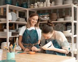 Frau, die Keramikkeramik herstellt. Attraktive, qualifizierte junge Dame in Schürze, die am Tisch steht und unterrichtet foto