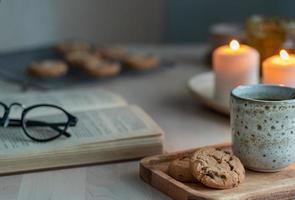 Lesebuch am gemütlichen Winterabend mit Kerzen, Tee und Keksen.