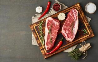 rohes Steak mit Salz, Thymian, Knoblauch würzen. zwei große ganze Stücke rohes Rindfleisch foto