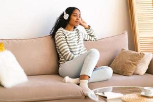 afroamerikanische frau, die hörbuch in kopfhörern hört, während sie auf dem sofa im wohnzimmer chillt foto