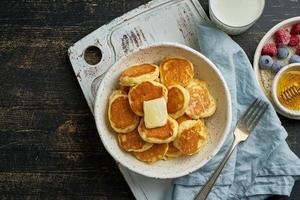 Pfannkuchen Müsli, winzige dünne lustige Crumpet, Kinderessen. frühstück mit getränk, dunkler tisch foto