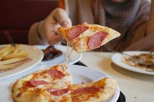 Frauen pflücken mit der Hand ein Stück Pizza von einem Teller foto