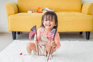 süßes kleines mädchen mit einer kleinen nationalflagge der vereinigten staaten, kindermädchen, das im wohnzimmer spielt foto