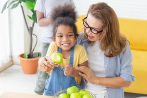 kind isst grüne apfelfrucht, großmutter und enkelkinder mit apfel im wohnzimmer foto
