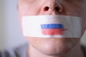 ein mit Klebeband verklebter Mund mit einer russischen Flagge, der versucht zu sagen. foto