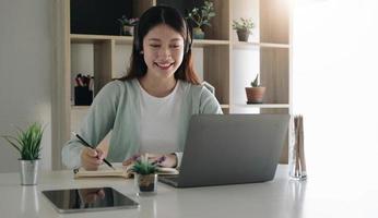 asiatische schulmädchen in lässiger kleidung liest und macht hausaufgaben videokonferenz e-learning mit lehrer auf laptop-computer zu hause foto