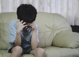 kleiner asiatischer Junge mit Brille mit der Hand auf dem Kopf, Kopfschmerzen wegen Stress. er traurig mit Migräne leiden. foto