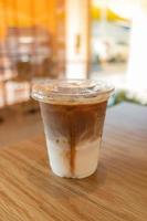Kalt gebrühter Latte-Eiskaffee, der in einer Schicht getrennt die Unterseite als Milchoberseite durch Kaffeeschuss in einem Plastikglas auf Holztisch im Restaurant und Café zeigt foto