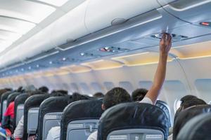 asiatisches paar personen kabinenbesatzung, hand hoch, um die konsolenplatte der klimaanlage einzustellen, lichtlampe über dem sitz der low-cost-airline. foto