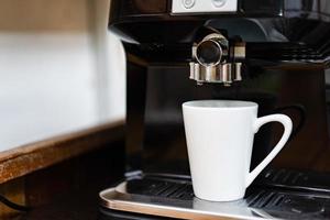 weiße Kaffeetasse Standby auf der professionellen Kaffeemaschine bereit, frischen heißen Kaffee zuzubereiten. foto