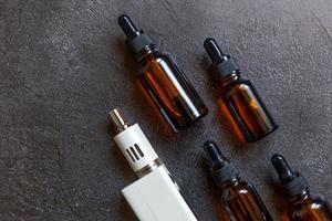 dampfgerät e-zigarette elektronische zigarette und flüssigkeitsflaschen auf dunkelschwarzem steinschieferhintergrund. Vape-Gerät für alternatives Rauchen. Vaping-Shop-Konzept. Gerät für Dampfer. Dampfzubehör. foto