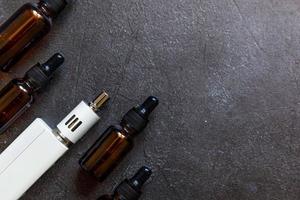 dampfgerät e-zigarette elektronische zigarette und flüssigkeitsflaschen auf dunkelschwarzem steinschieferhintergrund. Vape-Gerät für alternatives Rauchen. Vaping-Shop-Konzept. Gerät für Dampfer. Dampfzubehör. foto