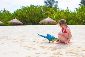entzückendes kleines Mädchen am Strand mit buntem Papagei foto