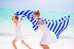 Kleine Mädchen haben Spaß beim Laufen mit Handtüchern am tropischen Strand mit weißem Sand und türkisfarbenem Meerwasser foto