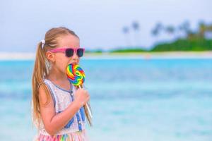 entzückendes kleines Mädchen mit Lutscher am tropischen Strand foto