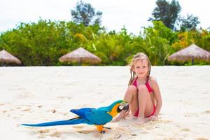 entzückendes kleines Mädchen am Strand mit buntem Papagei foto