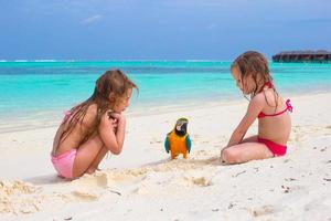 entzückende kleine Mädchen am Strand mit buntem Papagei foto
