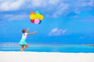 entzückendes kleines mädchen, das mit luftballons am strand spielt foto