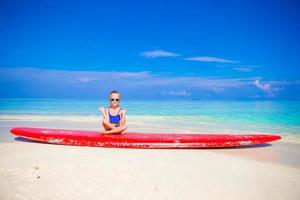 kleines Mädchen in Yoga-Position meditiert auf Surfbrett foto