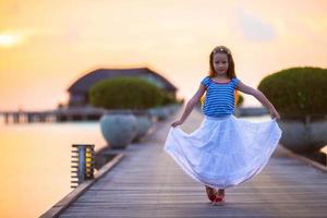 Silhouette eines entzückenden kleinen Mädchens auf einem Holzsteg bei Sonnenuntergang foto