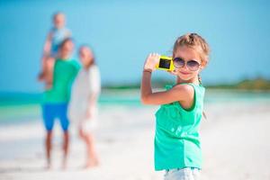 kleines Mädchen, das am Strand ein Foto der Familie macht