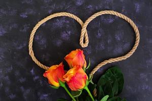 Herzform aus Seil und Rose auf dunklem Hintergrund. Ansicht von oben foto