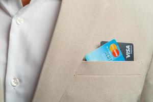 Geschäftsmann holt am 21.02.2022 Visa-Kreditkarten und Mastercard-Kreditkarten mit Fingern in brauner Anzugjacke und Details der Fasern des schönen Hintergrunds ab foto