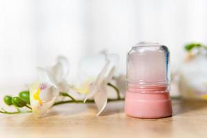 natürliches Öko-Kristall-Alaun-Deodorant und Orchideenzweig mit Blumen auf hellem Holzhintergrund foto